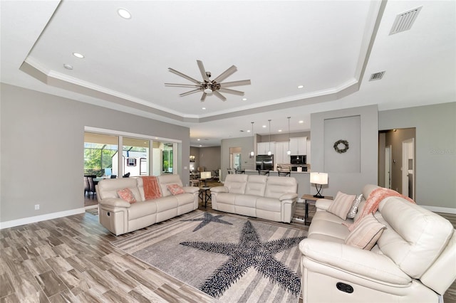 living area featuring visible vents, a raised ceiling, and baseboards