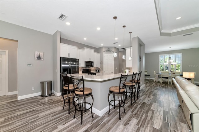 kitchen featuring a breakfast bar, white cabinetry, black appliances, and light wood-type flooring