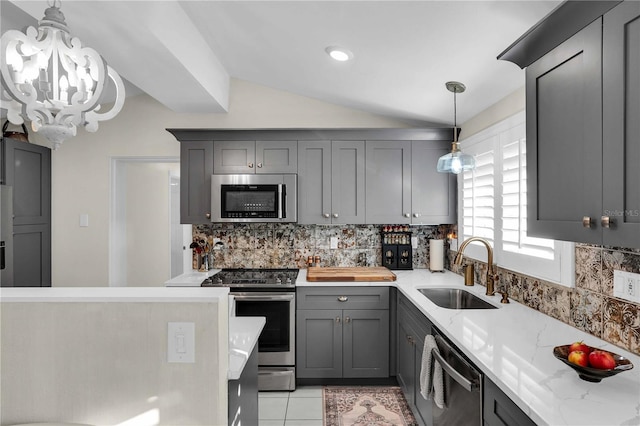 kitchen with gray cabinets, a sink, vaulted ceiling, appliances with stainless steel finishes, and tasteful backsplash