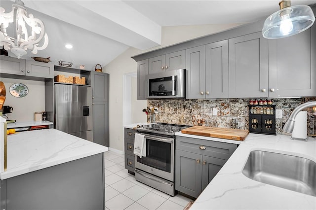 kitchen with backsplash, lofted ceiling, gray cabinets, appliances with stainless steel finishes, and a sink
