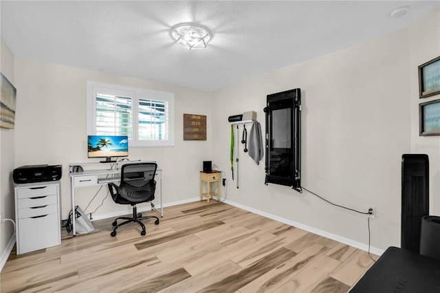 office space with baseboards, light wood-type flooring, and a textured ceiling