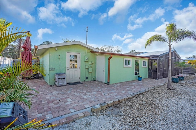 rear view of property with stucco siding, a patio, a lanai, and fence