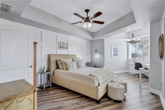 bedroom featuring a tray ceiling, a decorative wall, wood finished floors, and visible vents