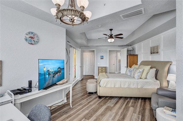 bedroom featuring a raised ceiling, visible vents, light wood finished floors, and a chandelier