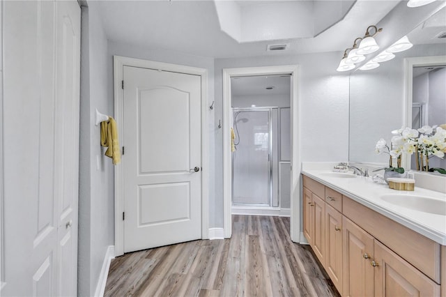 bathroom with wood finished floors, visible vents, double vanity, a sink, and a shower stall