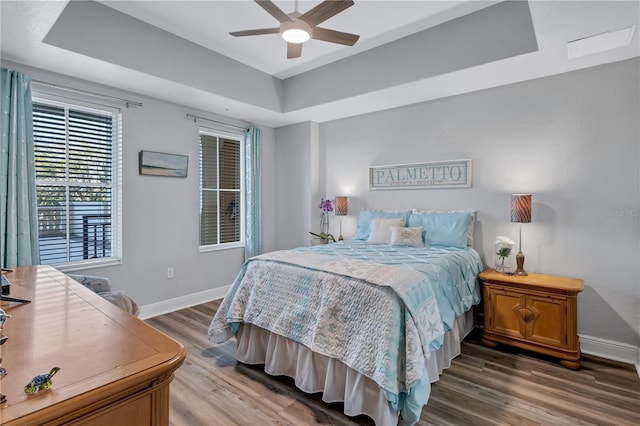 bedroom with ceiling fan, a raised ceiling, baseboards, and wood finished floors