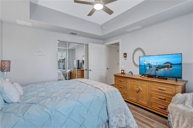 bedroom featuring visible vents, light wood-type flooring, a tray ceiling, a closet, and a ceiling fan