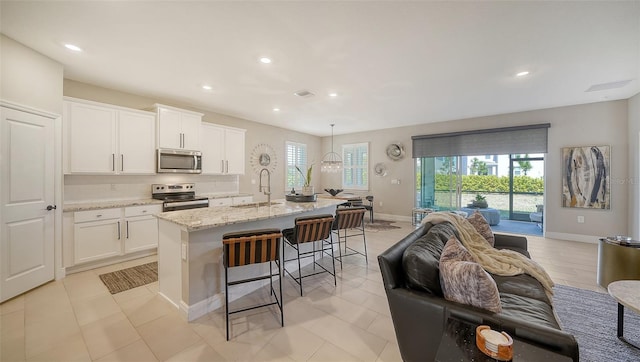 kitchen featuring a sink, light stone counters, a kitchen breakfast bar, open floor plan, and appliances with stainless steel finishes