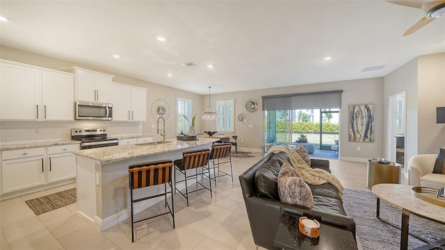 kitchen with tasteful backsplash, open floor plan, light stone counters, stainless steel appliances, and a sink