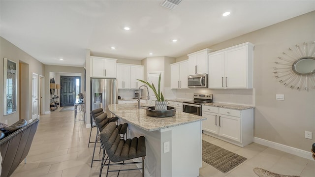 kitchen featuring light stone counters, visible vents, a breakfast bar, stainless steel appliances, and white cabinets