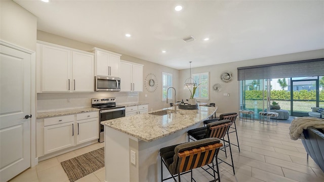 kitchen featuring visible vents, a sink, decorative backsplash, appliances with stainless steel finishes, and a kitchen island with sink