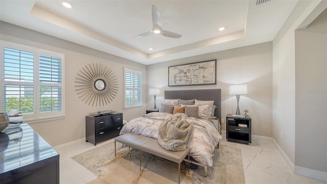 bedroom with a tray ceiling, multiple windows, and baseboards