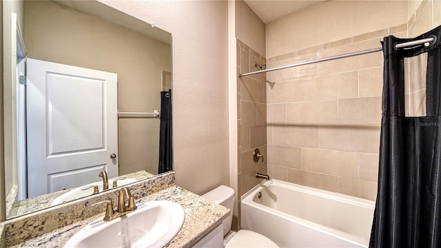 bathroom featuring vanity, toilet, a textured wall, and shower / bath combo