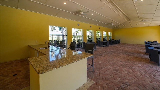 interior space featuring a sink, stone countertops, brick floor, lofted ceiling, and ceiling fan