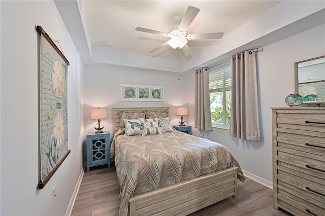 bedroom with ceiling fan, a raised ceiling, baseboards, and wood finished floors