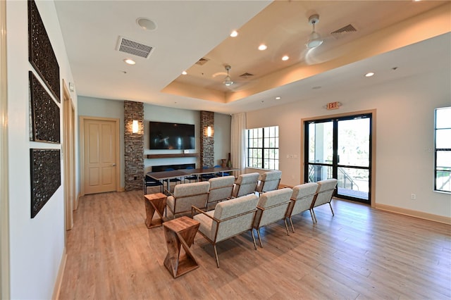 living room with visible vents, a fireplace, ceiling fan, light wood-style floors, and a raised ceiling