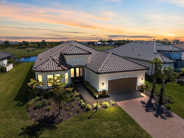 mediterranean / spanish house featuring a front lawn, a tile roof, stucco siding, decorative driveway, and an attached garage