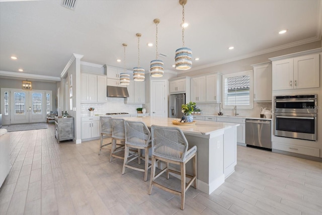 kitchen featuring under cabinet range hood, a sink, a kitchen breakfast bar, a center island, and stainless steel appliances