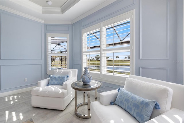 sitting room featuring a tray ceiling, wood finished floors, ornamental molding, and a decorative wall