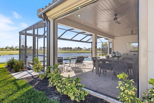 view of patio / terrace featuring glass enclosure, outdoor dining space, a water view, and ceiling fan