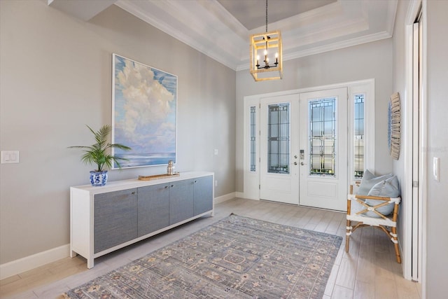 foyer entrance featuring baseboards, a raised ceiling, light wood-style flooring, and ornamental molding