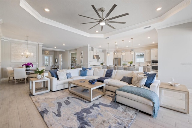 living room with light wood finished floors, visible vents, crown molding, and a tray ceiling