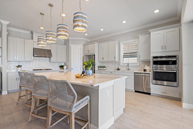 kitchen featuring a kitchen island, under cabinet range hood, a kitchen bar, stainless steel appliances, and a sink