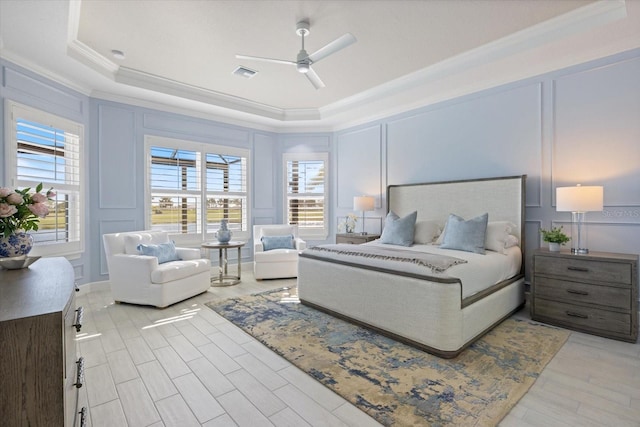 bedroom featuring visible vents, a tray ceiling, light wood-style floors, crown molding, and a decorative wall