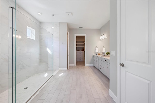 full bath with a marble finish shower, a walk in closet, baseboards, wood finished floors, and vanity