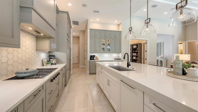 kitchen featuring visible vents, custom range hood, a sink, light countertops, and glass insert cabinets