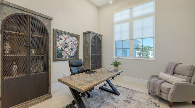 home office featuring light tile patterned flooring, a high ceiling, and baseboards