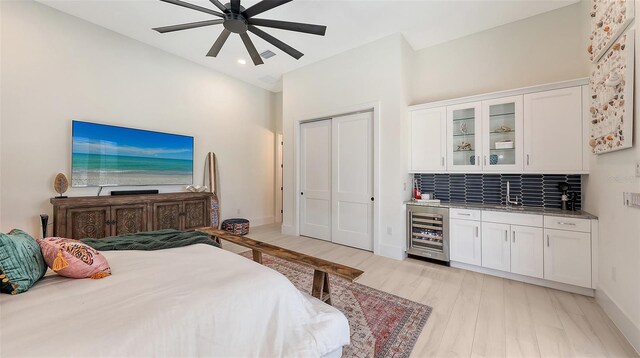 bedroom featuring light wood finished floors, baseboards, wine cooler, a closet, and a ceiling fan