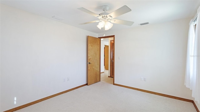 spare room featuring visible vents, light colored carpet, a ceiling fan, and baseboards