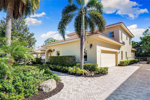 view of property exterior featuring stucco siding, a tile roof, decorative driveway, fence, and an attached garage