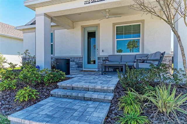 view of exterior entry with an outdoor living space, stucco siding, stone siding, and a ceiling fan