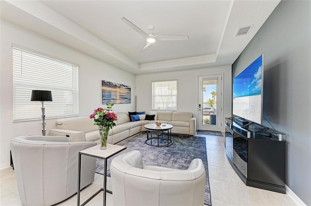 living area with baseboards, visible vents, a tray ceiling, light tile patterned flooring, and ceiling fan