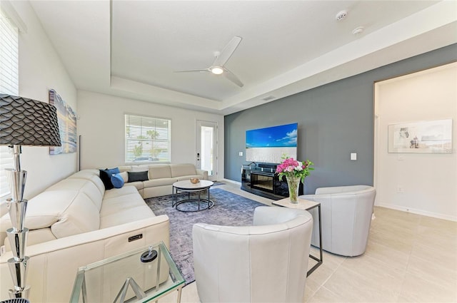 living room featuring light tile patterned floors, a tray ceiling, baseboards, and a ceiling fan