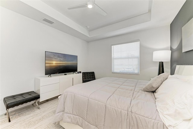 bedroom with light wood-type flooring, visible vents, a raised ceiling, and a ceiling fan