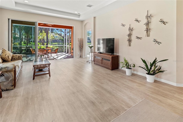 living room featuring visible vents, light wood-type flooring, and a tray ceiling