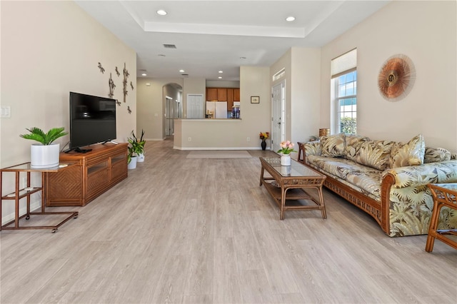 living area with a tray ceiling, arched walkways, baseboards, and light wood-style flooring