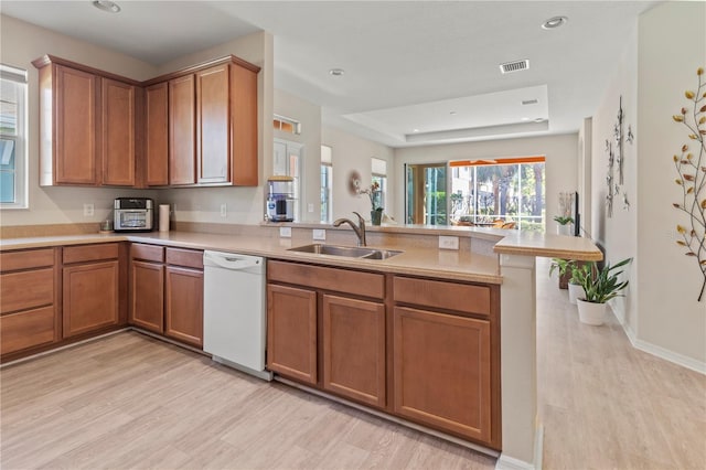 kitchen featuring visible vents, a sink, a peninsula, brown cabinetry, and white dishwasher