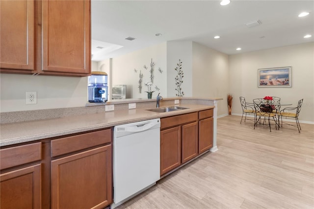 kitchen with brown cabinetry, a peninsula, white dishwasher, a sink, and light wood-type flooring