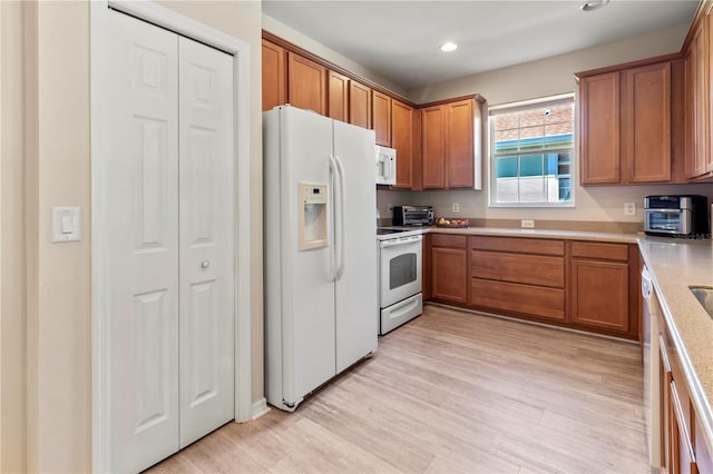 kitchen featuring white appliances, brown cabinetry, light wood-style floors, and light countertops