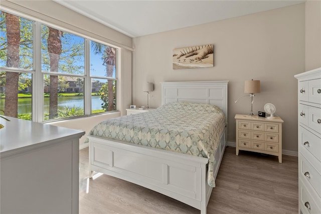 bedroom with light wood finished floors, baseboards, and a water view