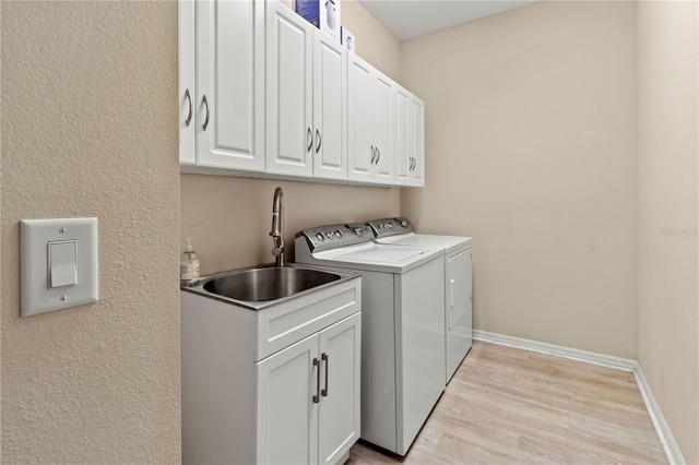 laundry area featuring baseboards, washing machine and clothes dryer, cabinet space, a sink, and light wood-style floors