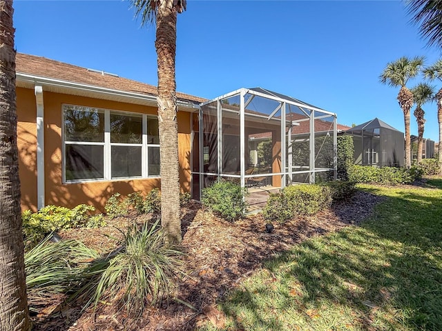 rear view of house with glass enclosure, a lawn, and stucco siding