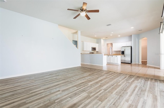 unfurnished living room featuring visible vents, baseboards, arched walkways, ceiling fan, and light wood-type flooring