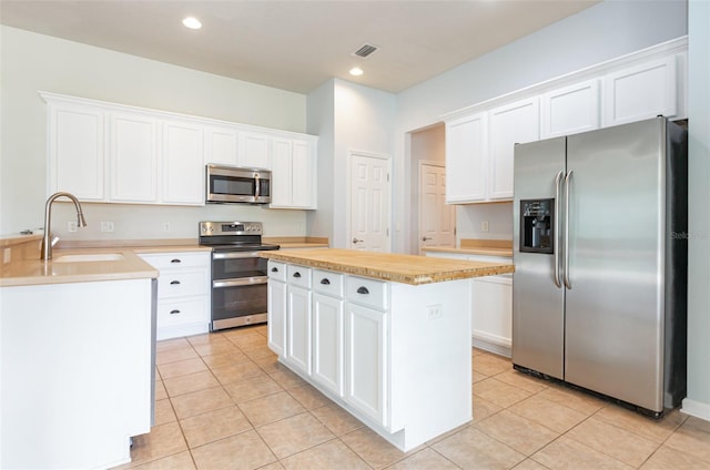 kitchen with light tile patterned floors, white cabinets, appliances with stainless steel finishes, and a sink