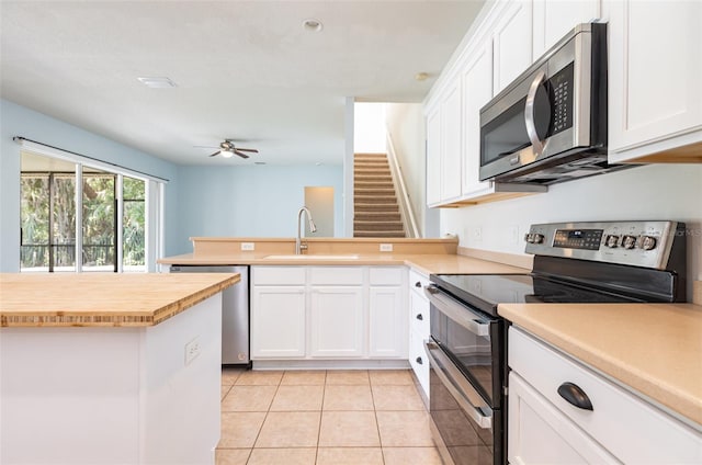 kitchen with a peninsula, stainless steel appliances, light tile patterned flooring, white cabinetry, and a sink