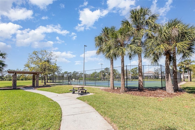 view of home's community featuring a tennis court, a lawn, and fence